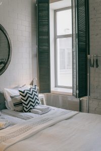 A cozy and stylish bedroom featuring modern decor and a sunlit window with shutter panels. Chambre douillette et élégante avec une décoration moderne et une fenêtre ensoleillée dotée de panneaux de volets.