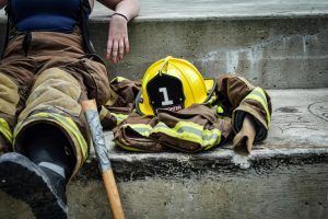 Pompière faisant une pause sur des marches en béton avec son équipement et son casque à proximité.