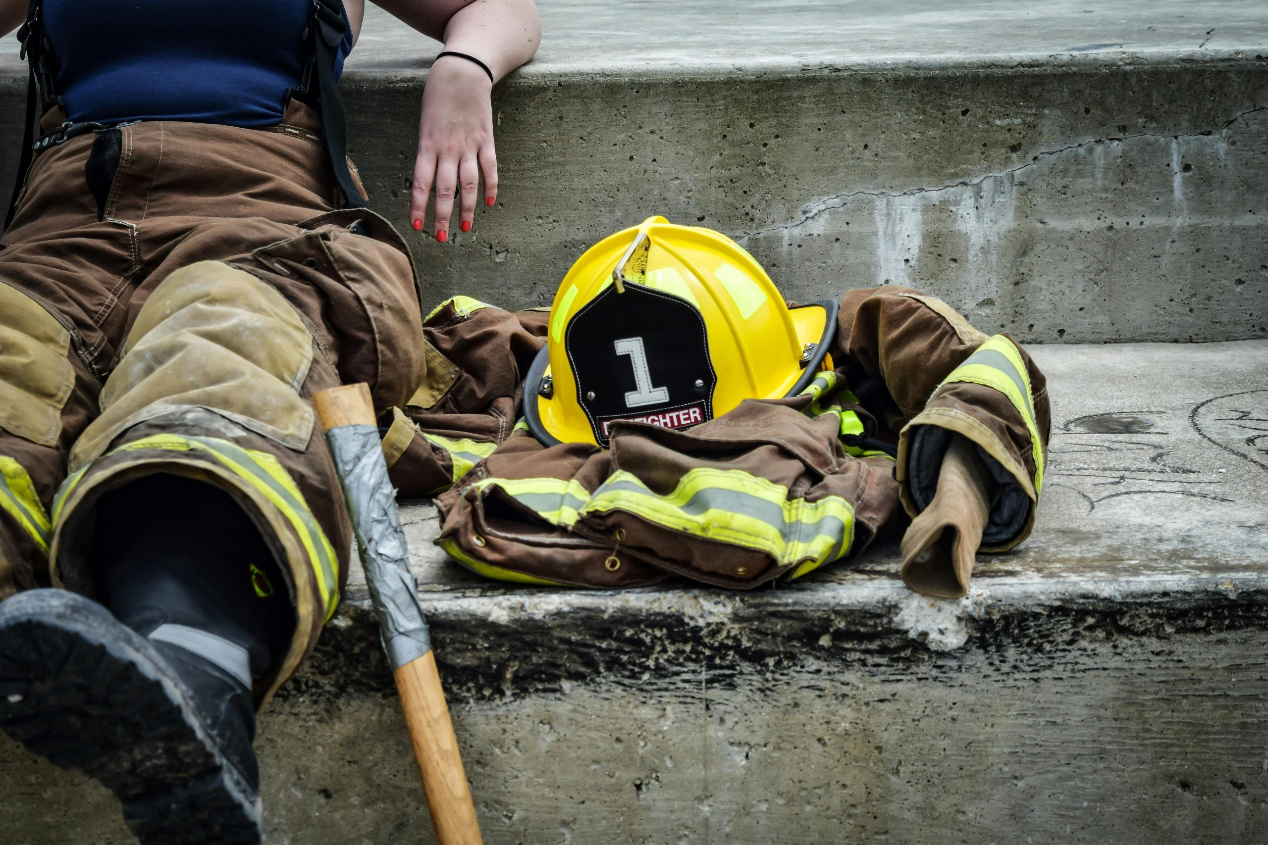 Pompière faisant une pause sur des marches en béton avec son équipement et son casque à proximité.