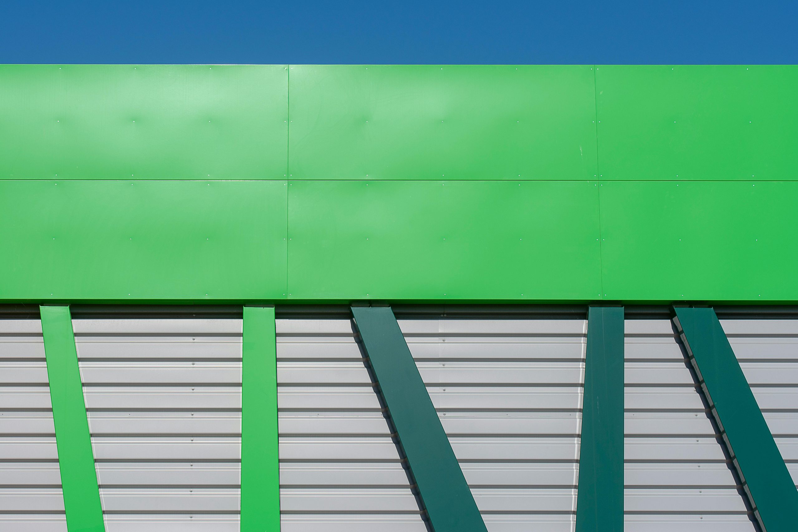 Close-up d'une façade de bâtiment industriel moderne verte avec un design géométrique sur un ciel bleu dégagé.