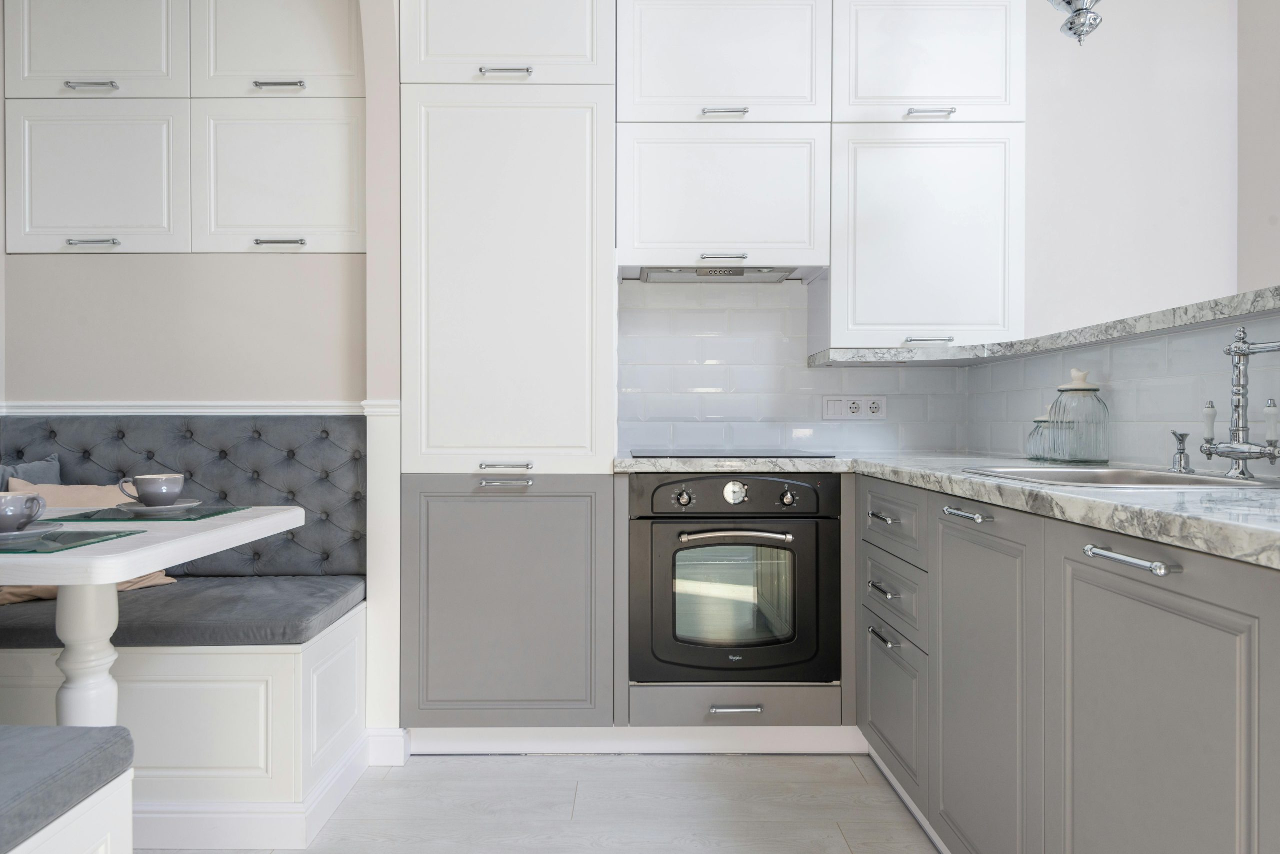 Salle à manger servie avec de la vaisselle placée près d'un comptoir de cuisine en marbre avec des placards blancs et gris et des ustensiles de cuisine modernes dans un appartement élégant.