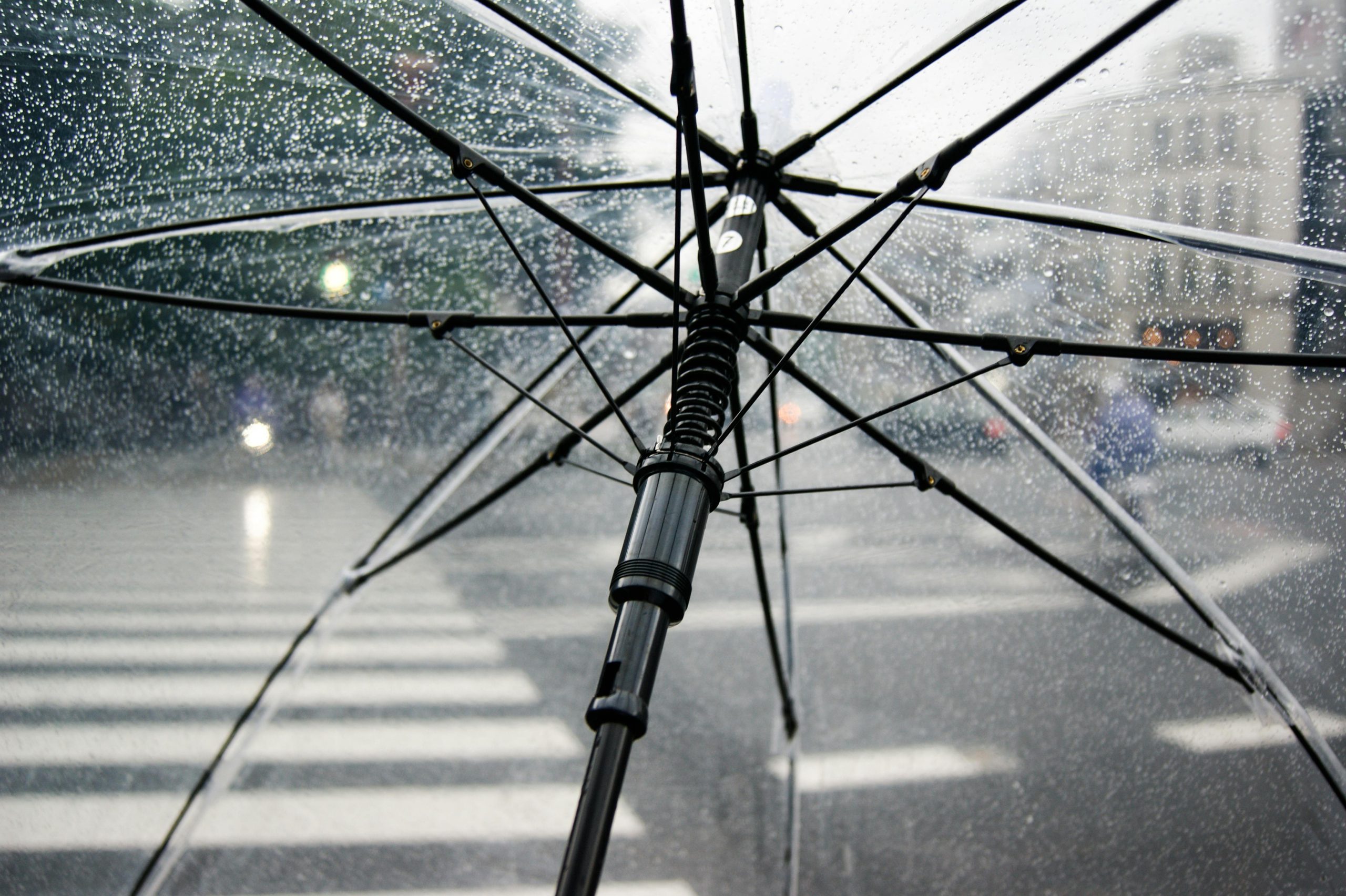 Gros plan d'un parapluie transparent avec des gouttes de pluie dans un cadre urbain.