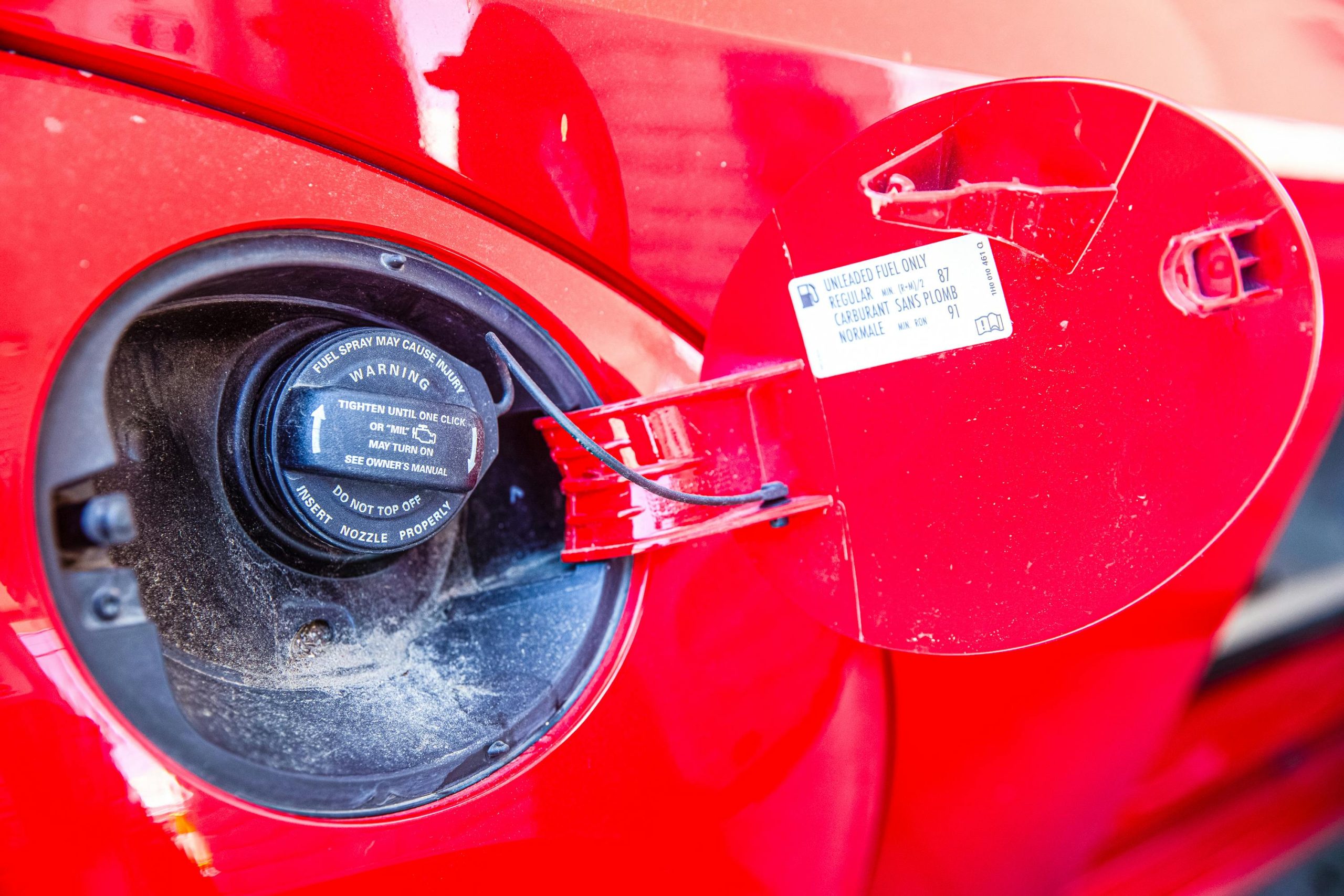 Détail du bouchon de réservoir et de l'étiquette d'avertissement d'une voiture rouge. Idéal pour les thèmes automobiles.