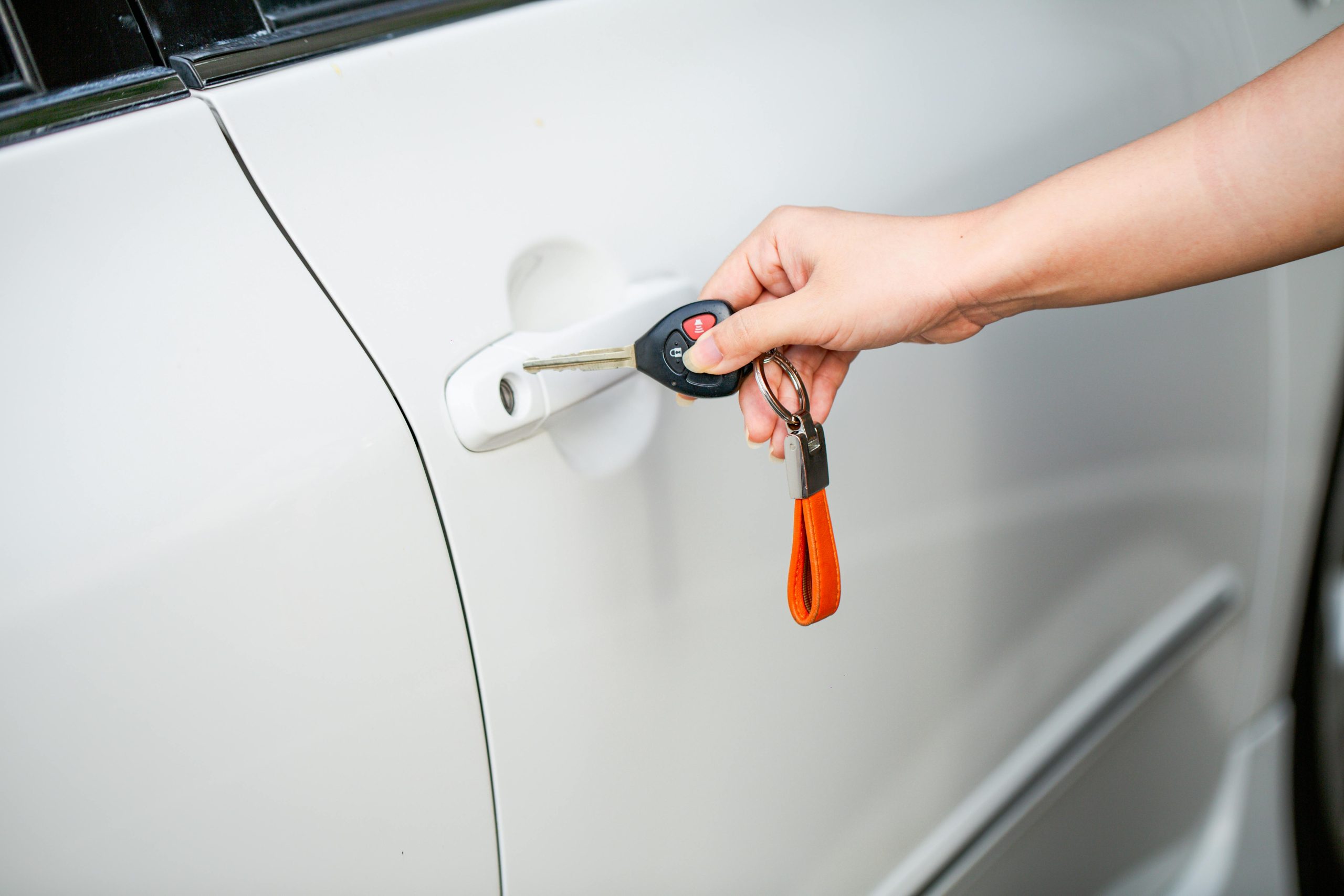 Close-up d'une main déverrouillant une portière de voiture blanche avec une clé métallique et un porte-clés.
