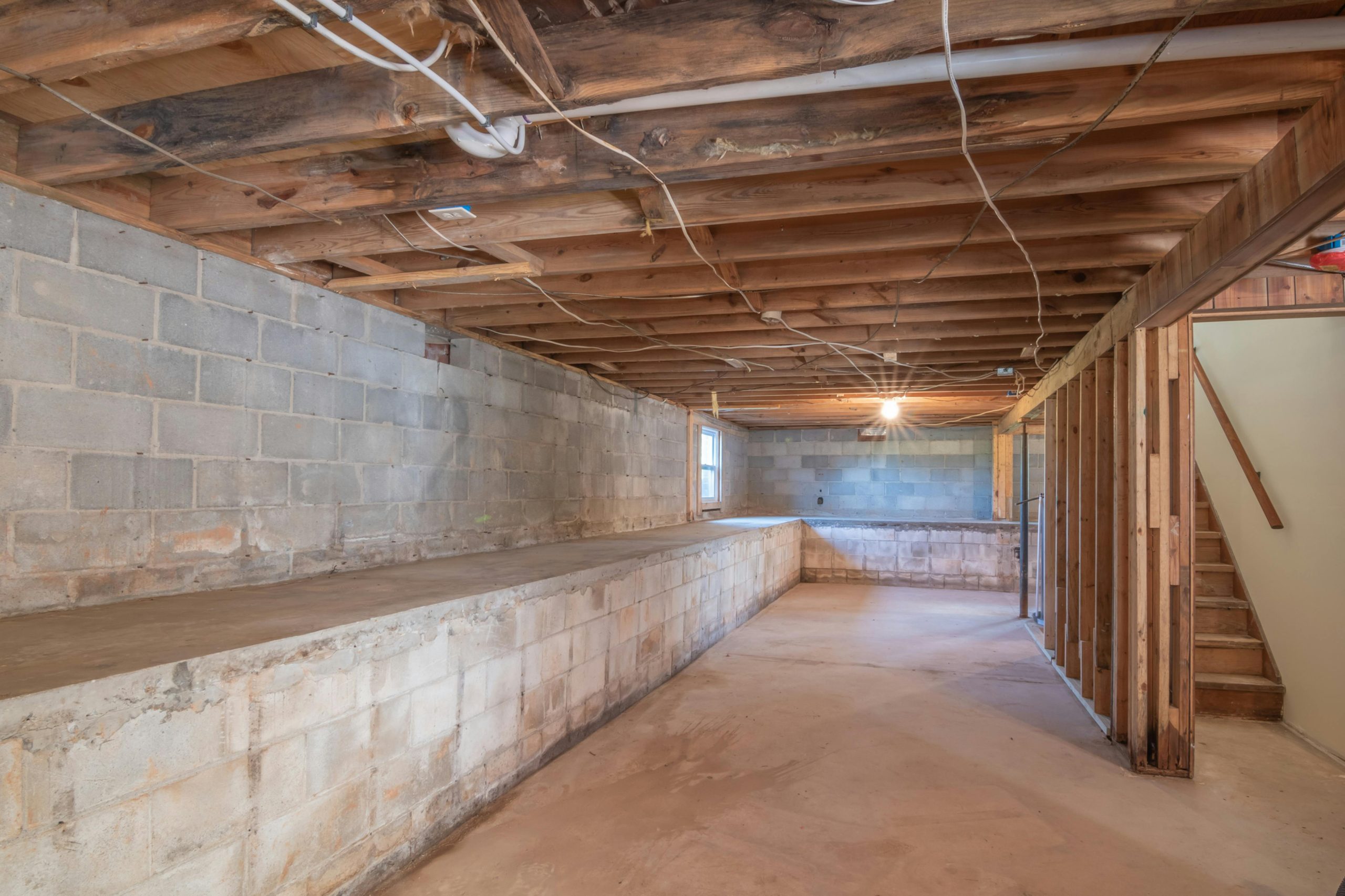 Cave vide avec poutres en bois apparentes, murs en béton et escaliers.