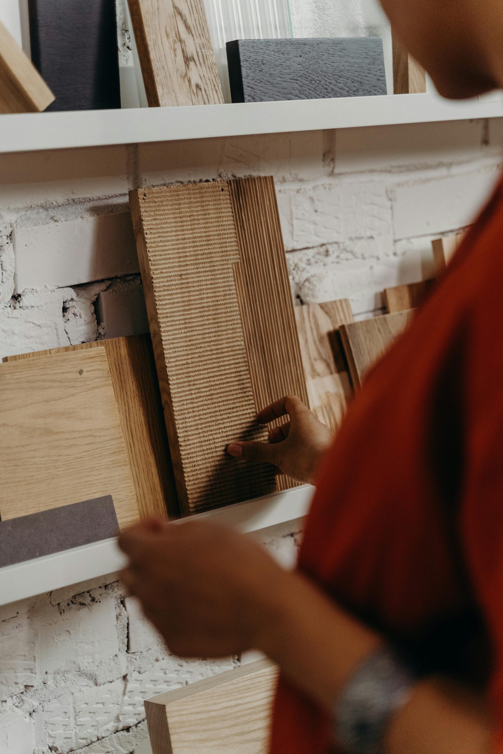 Close-up d'une personne sélectionnant des échantillons de matériaux en bois sur une étagère contre un mur en briques.